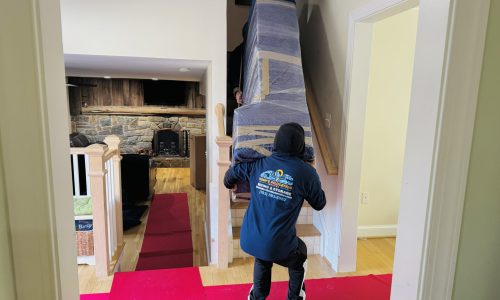 Movers carrying a large cabinet through the front entrance of a townhouse during a residential move